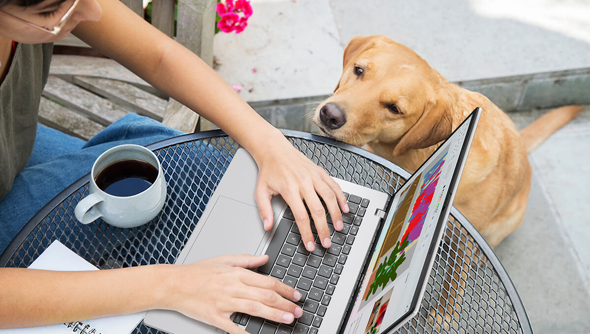 A woman is having coffee and using ASUS Vivobook on a table as a Labrador retriever sits beside her.