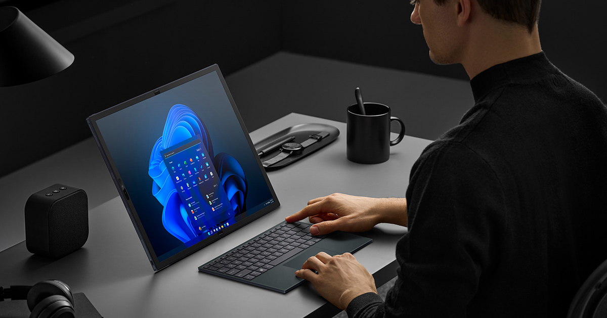  A man using Zenbook 17 Fold OLED with Windows 11 on the desk in a Desktop Mode, typing on the ErgoSense Bluetooth keyboard and touchpad, with black accessories also on the desk