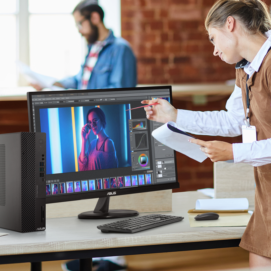 A designer is talking on a phone and pointing at the monitor which shows  photo editing.