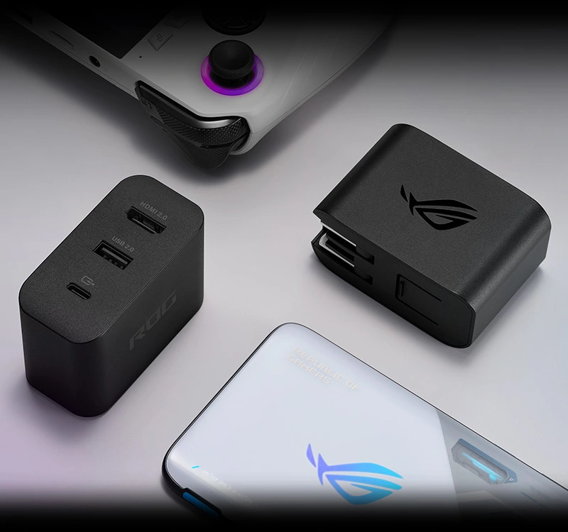 ROG Ally, dwie stacje ładujące Gaming Charger, kabel USB-C oraz ROG Phone 7 na białym stole.