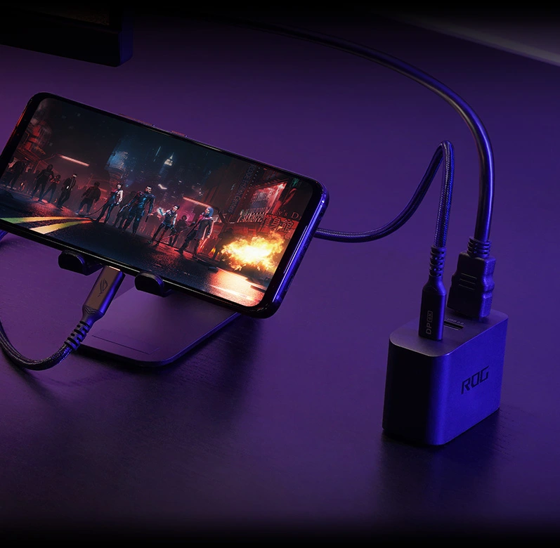 Telefon ROG Phone 7 podłączony przez port USB-C do ROG Gaming Charger Dock, z wyjściem HDMI dostarczającym sygnał do zewnętrznego monitora.