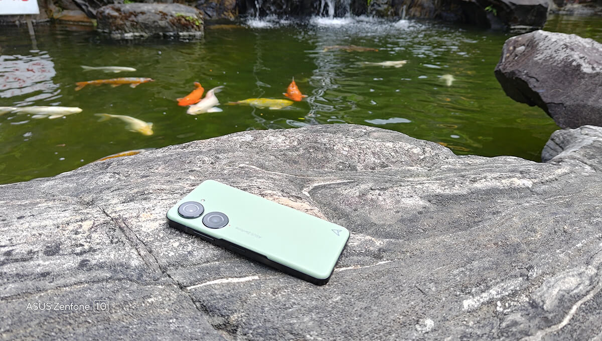 Zenfone 10 lying screen-down on a stone surface next to a pond with fish in it.