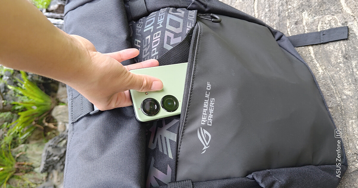 a hand holding a green Zenfone 10 while putting it into a front pocket of an ROG backpack.