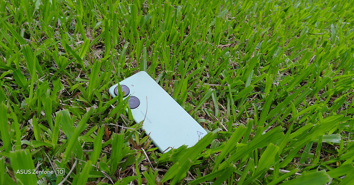 Green Zenfone 10 lying on the ground in green grass.