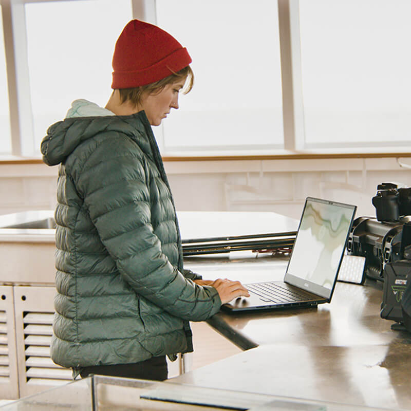 a woman using an ASUS ProArt Studiobook 16 OLED to quickly edit a video with camera equipment next to the laptop while on a boat’s bridge