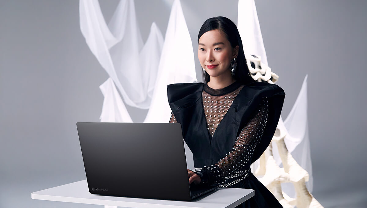 woman in black using a ProArt laptop on a white table with white drapes in the background.