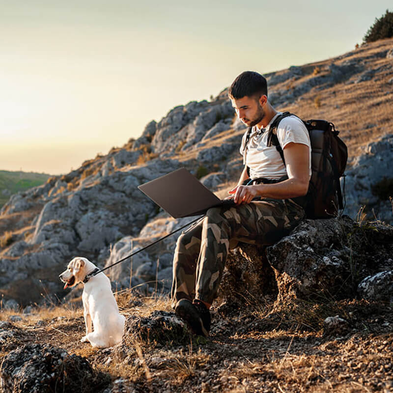 A man is using ProArt P16 while sitting on a rock beside a cliff.