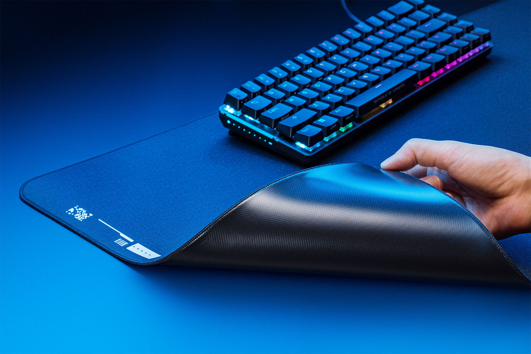 An image with a hand turning over a corner of the ROG Hone Ace XXL to show its base material