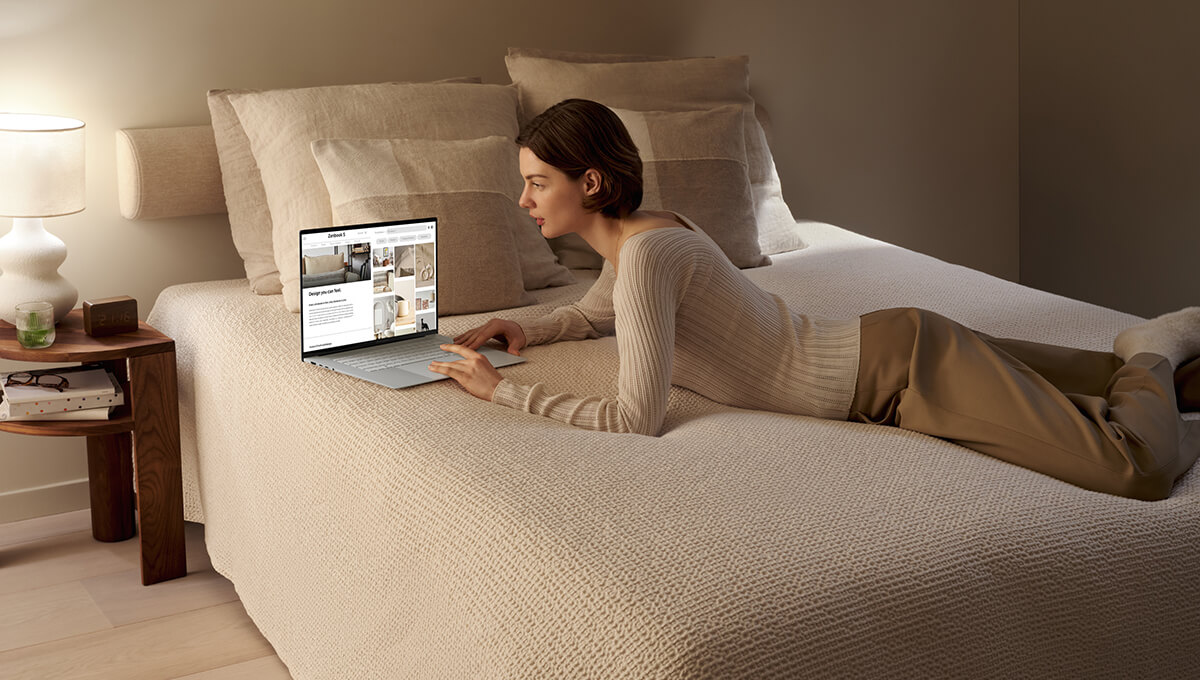 a woman lying on bed while using ASUS Zenbook S 16 laptop to browse internet