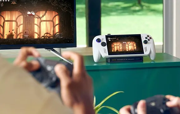 Una persona jugando con un controlador en la mano en un televisor, con la ROG Xbox Ally sentado cerca del televisor en un mostrador verde.