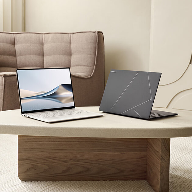 Two Zenbook S 16 laptops are placed on a beige colored table in a modern looking living room.