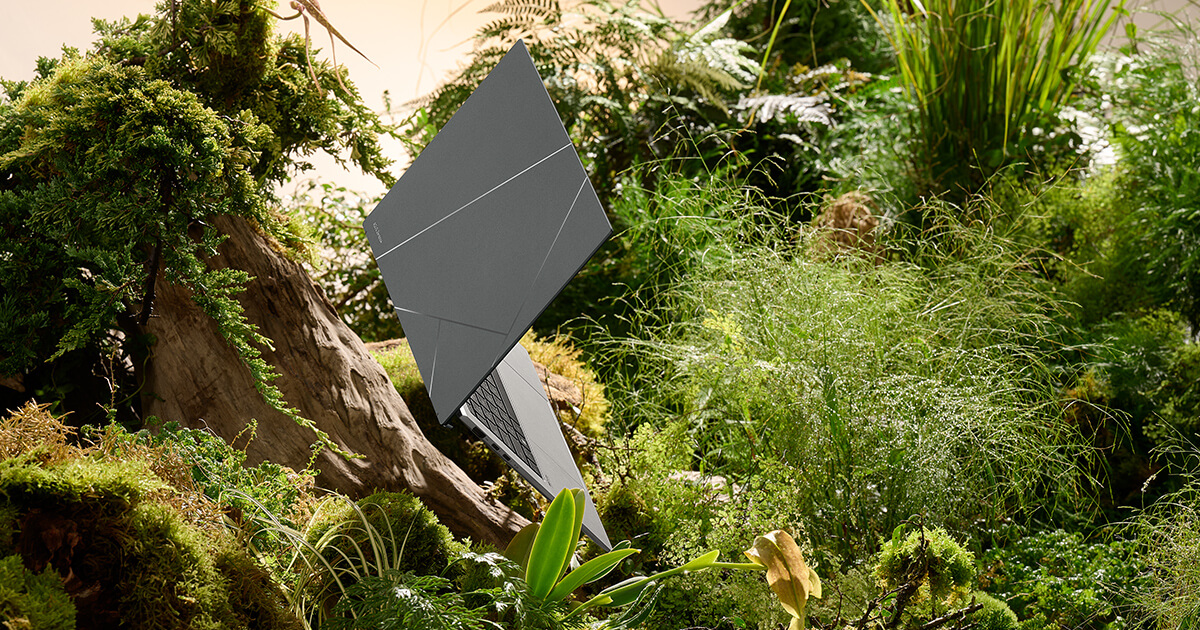 Zenbook S 13 OLED în modul stand este pe linia de plutire într-un mediu înconjurător sau înverzit. Bușteni, ferigi, iarbă și elemente ale naturii alcătuiesc fundalul.