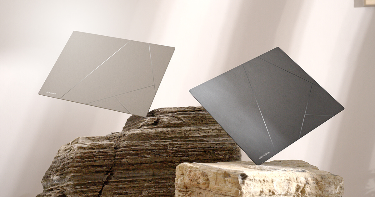 Two laptops are standing on their corners on two blocks of stone in front of a beige background. The one on the left is a sandstone beige laptop on top of a brown stone while the one on the right is a basalt grey laptop on a cream-colored stone.