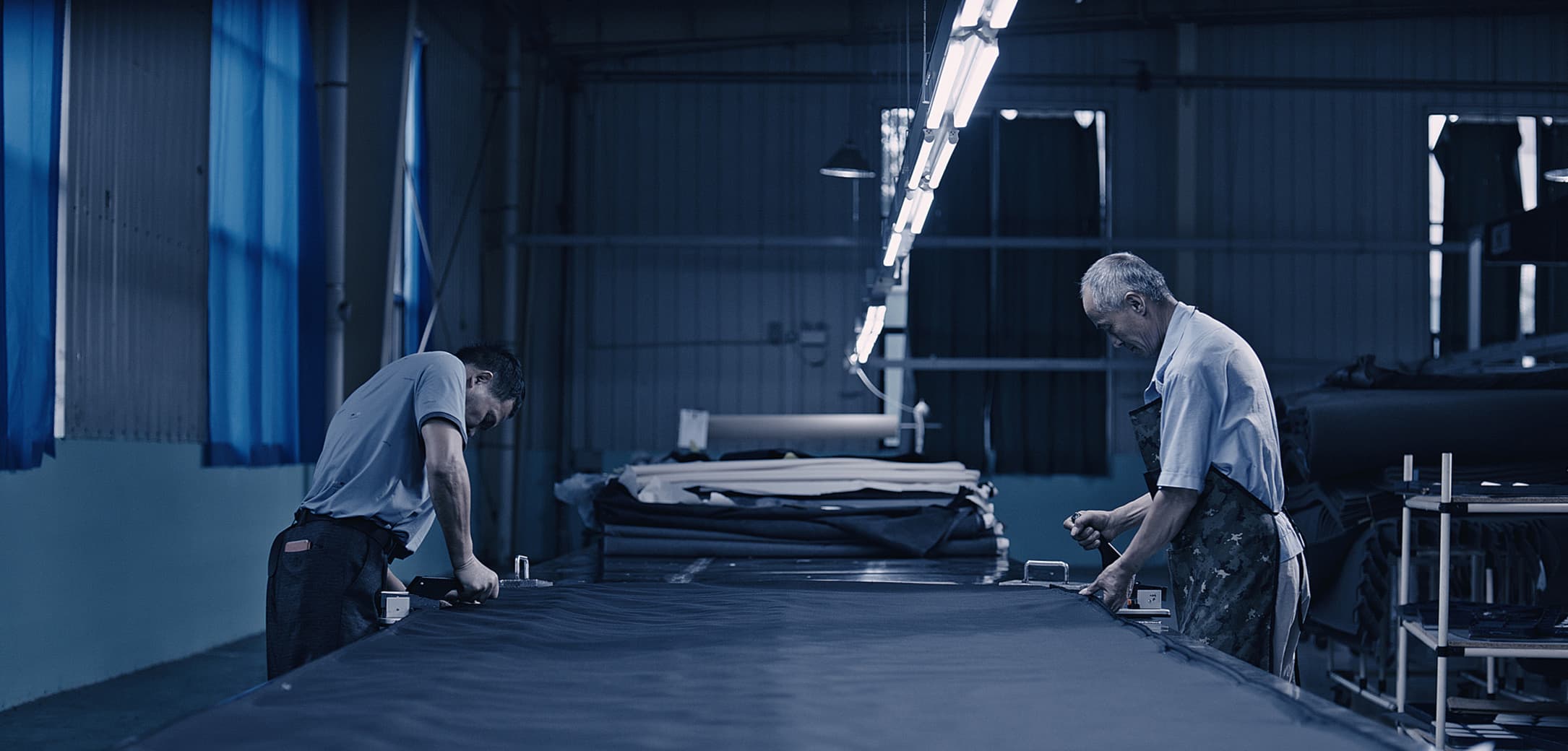 Man using a large cutting machine to precisely cut a piece of fabric in a textile factory.