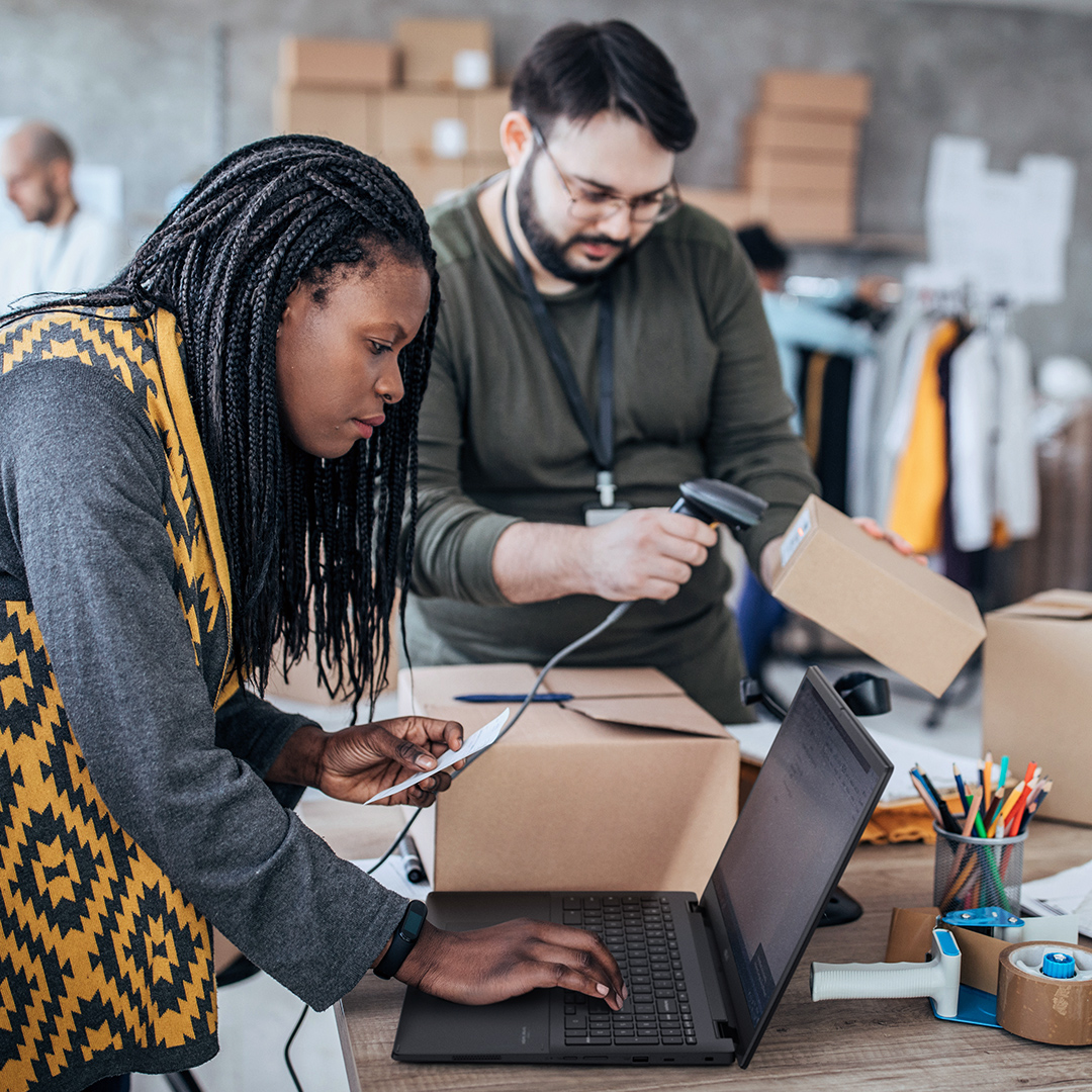 L'un des employés de la boutique en ligne vérifie les informations d'un Chromebook ASUS et un autre scanne le code-barres de l'emballage.