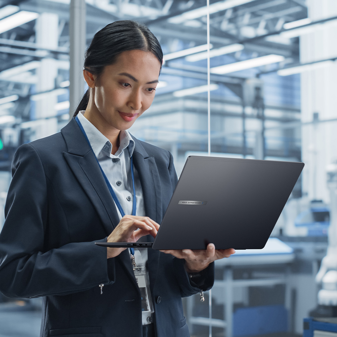 A business lady is looking at an ASUS ExpertBook's monitor on her hand in a factory