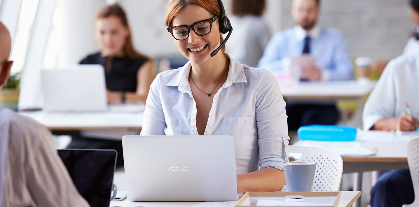 Zaměstnanec zákaznické linky telefonuje se sluchátky nad notebookem ASUS.