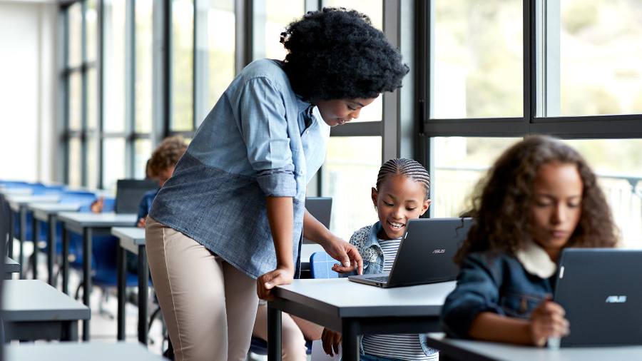 Kinderen gebruiken hun eigen ASUS BR1100-laptop in de klas en een docent geeft les aan een meisje, terwijl ze samen naar de laptop kijken.