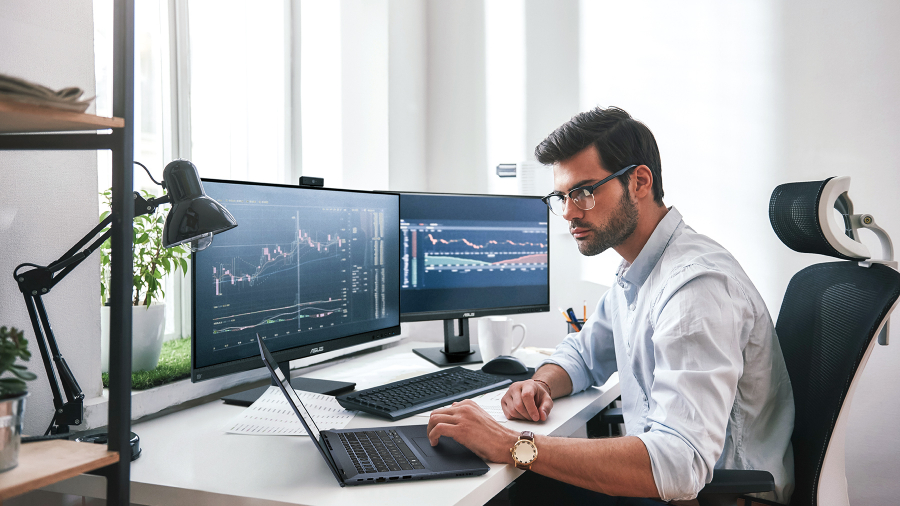 Een man volgt realtime informatie over de aandelenmarkt via een ASUS ExpertBook-laptop met twee monitoren op het bureau.