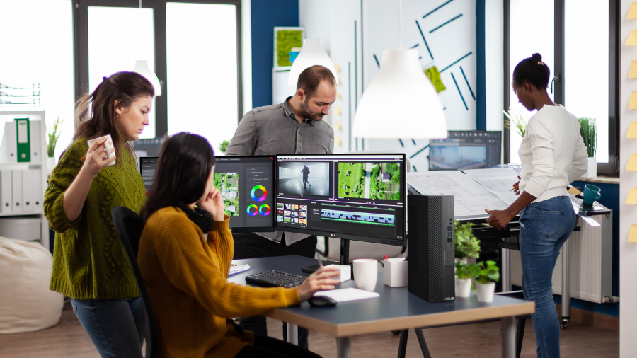 Vier creatieve medewerkers zijn aan het werk op kantoor en twee van hen bespreken samen een videobewerking met een ASUS ExpertCenter-desktop en ProArt-monitoren op het bureau.