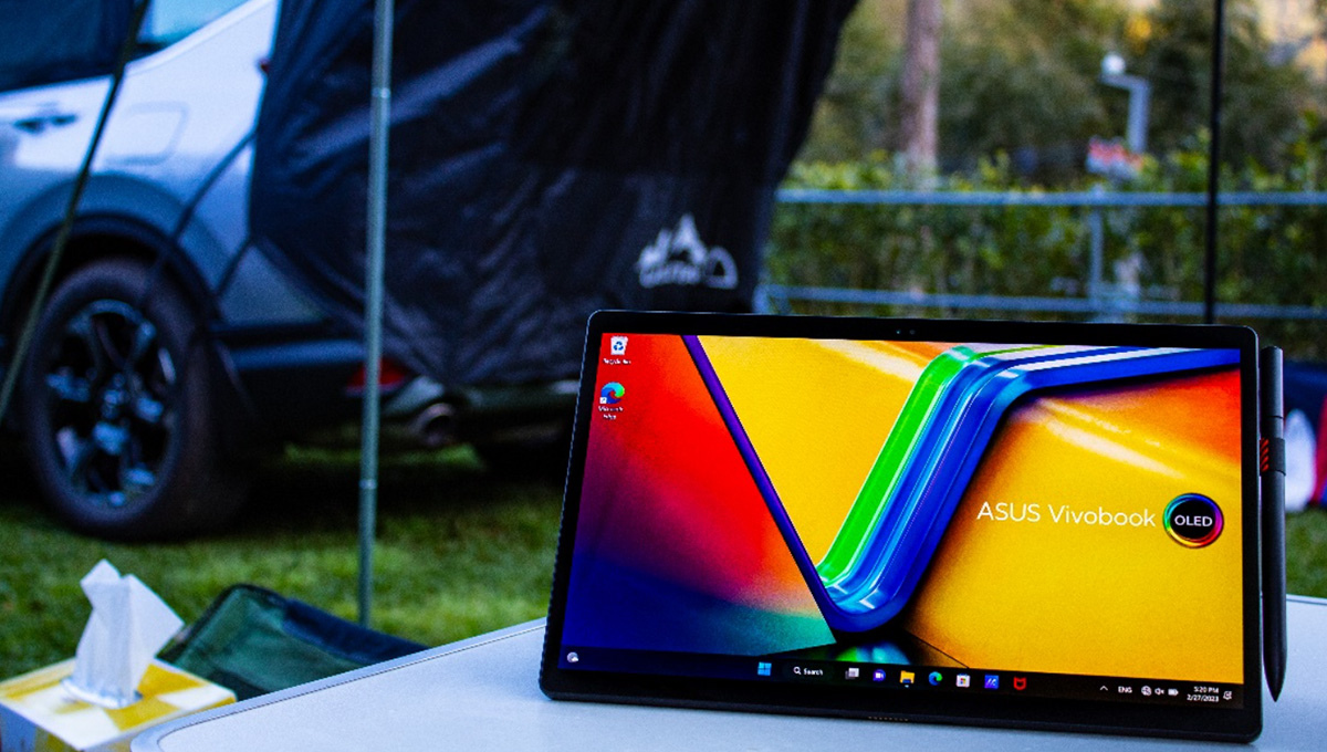ASUS Vivobook 13 Slate OLED convertible laptop in a stand mode with a colorful wallpaper on a camping table with a car and a tent in the background