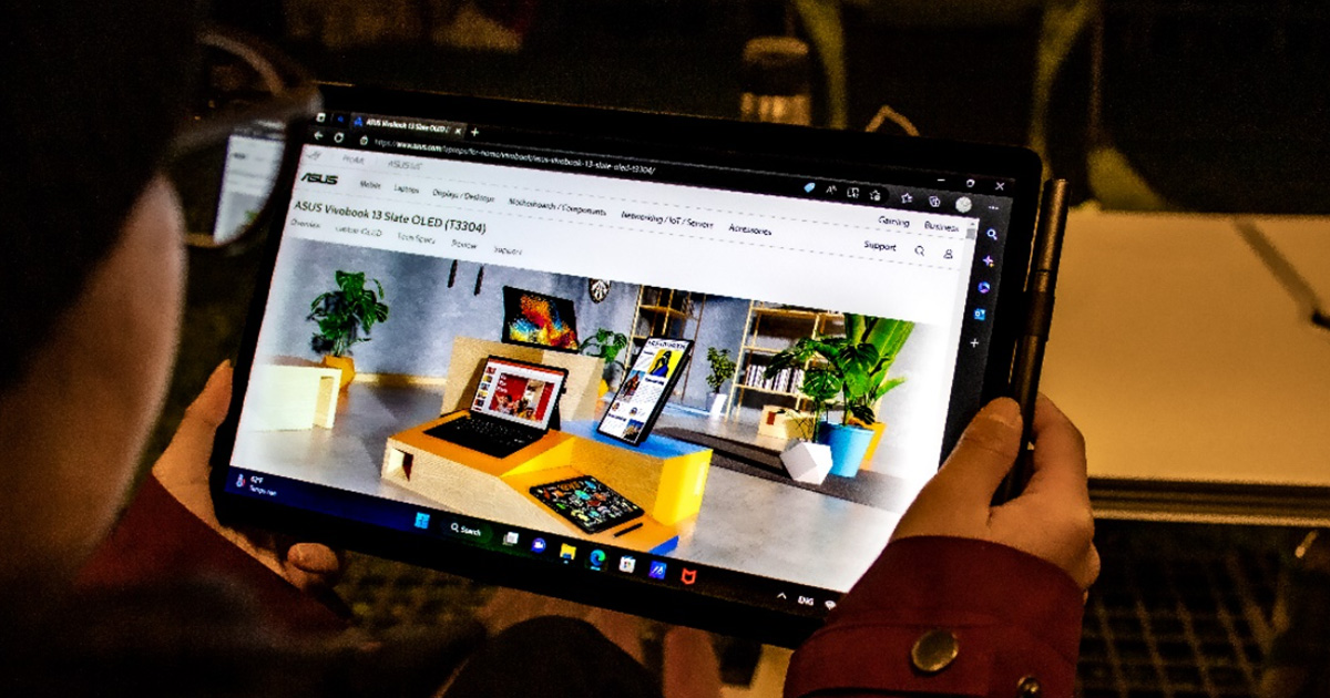 A woman holding ASUS Vivobook 13 Slate OLED convertible laptop in two hands horizontally in tablet mode, with a website displayed on the screen
