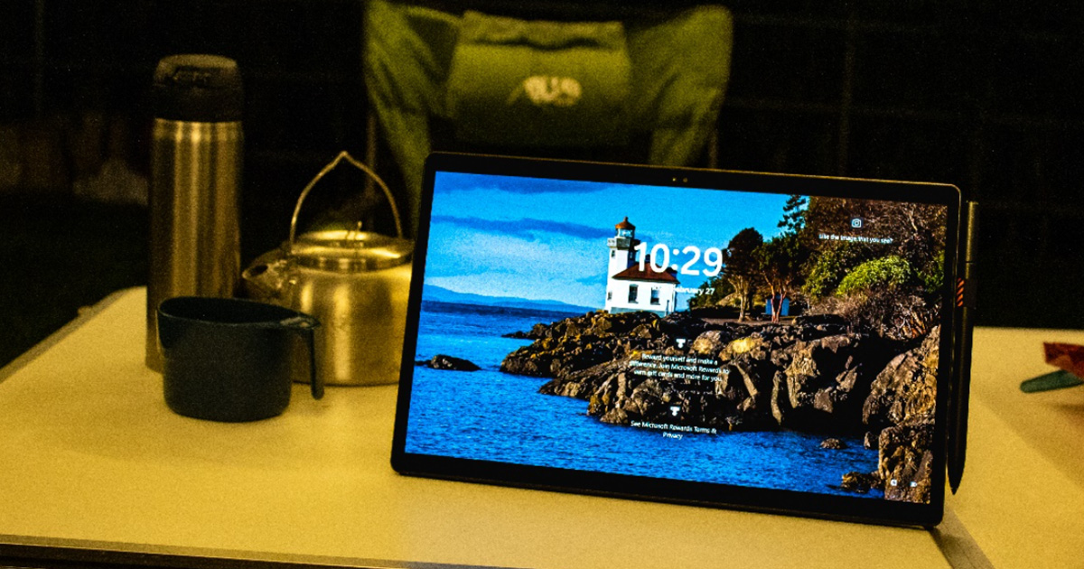 The lock screen on an ASUS Vivobook 13 Slate OLED convertible laptop in horizontal stand mode on a camping table with camping equipment and chair in the background