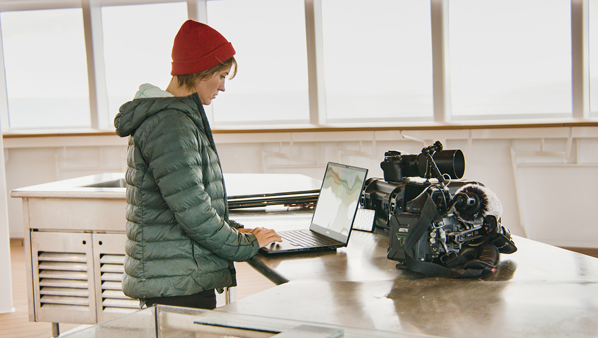 a woman using an ASUS ProArt Studiobook 16 OLED to quickly edit a video with camera equipment next to the laptop while on a boat’s bridge