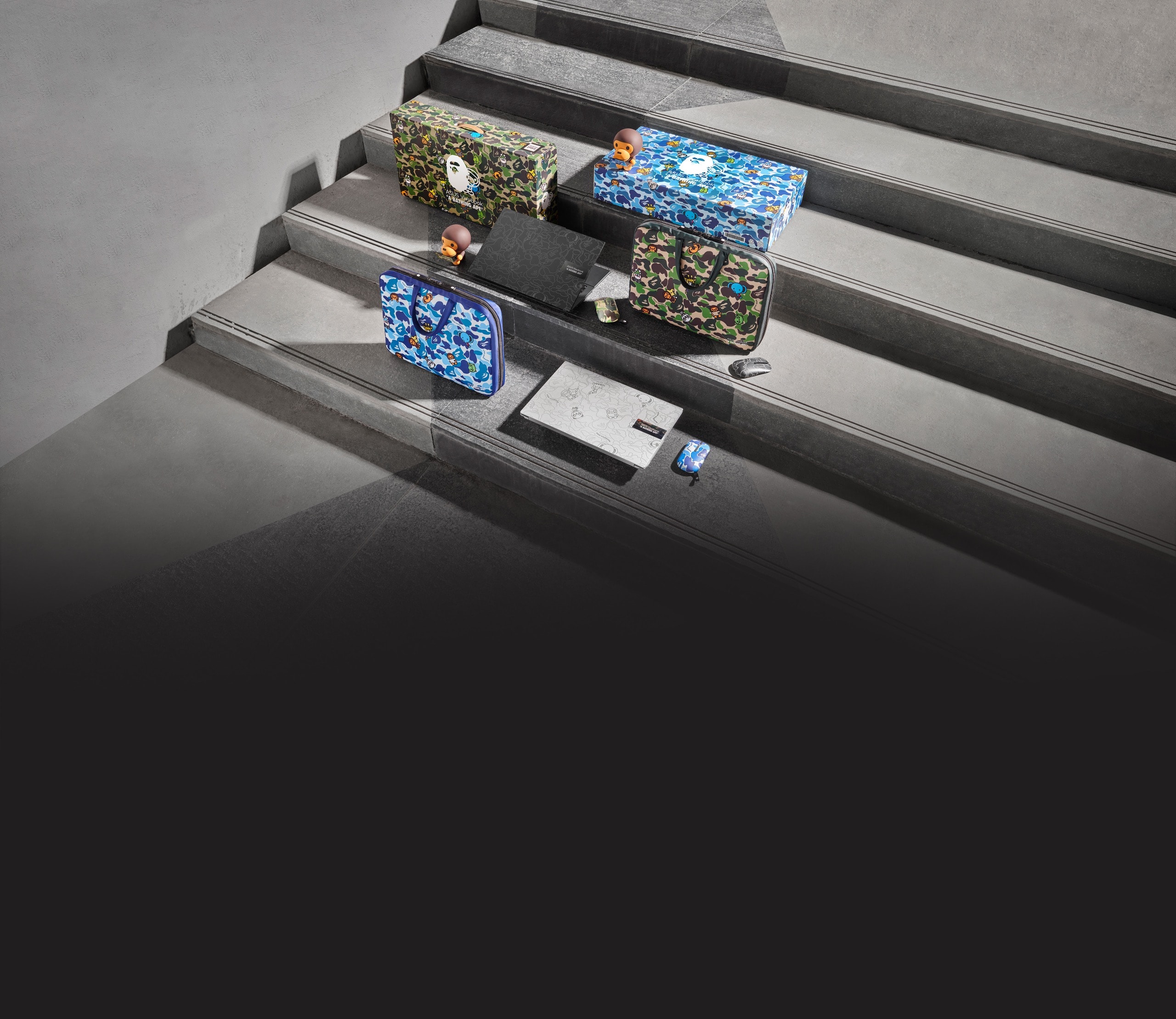 As embalagens do Vivobook BAPE Edition azuis e verdes expostos em escadas cinzentas, incluindo a caixas de oferta, portáteis, ratos e malas de transporte.