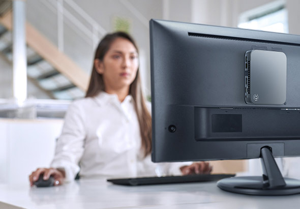 A woman in white shirt staring at ASUS display monitor with a NUC 14 Essential VESA-mounted to the back of the monitor.