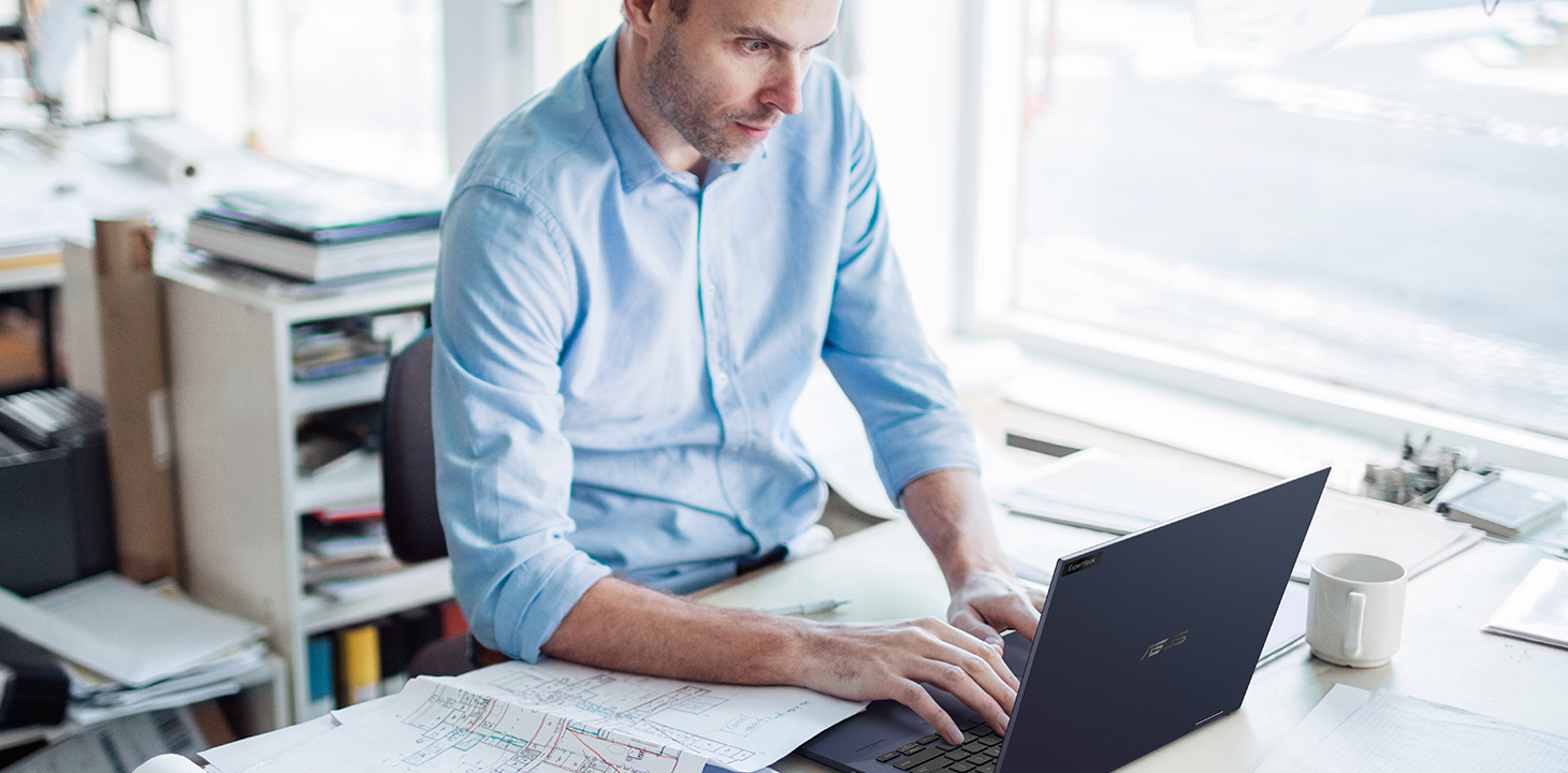 Un uomo d'affari sta guardando con attenzione il suo ASUS ExpertBook e sulla scrivania c'è un progetto di costruzione.