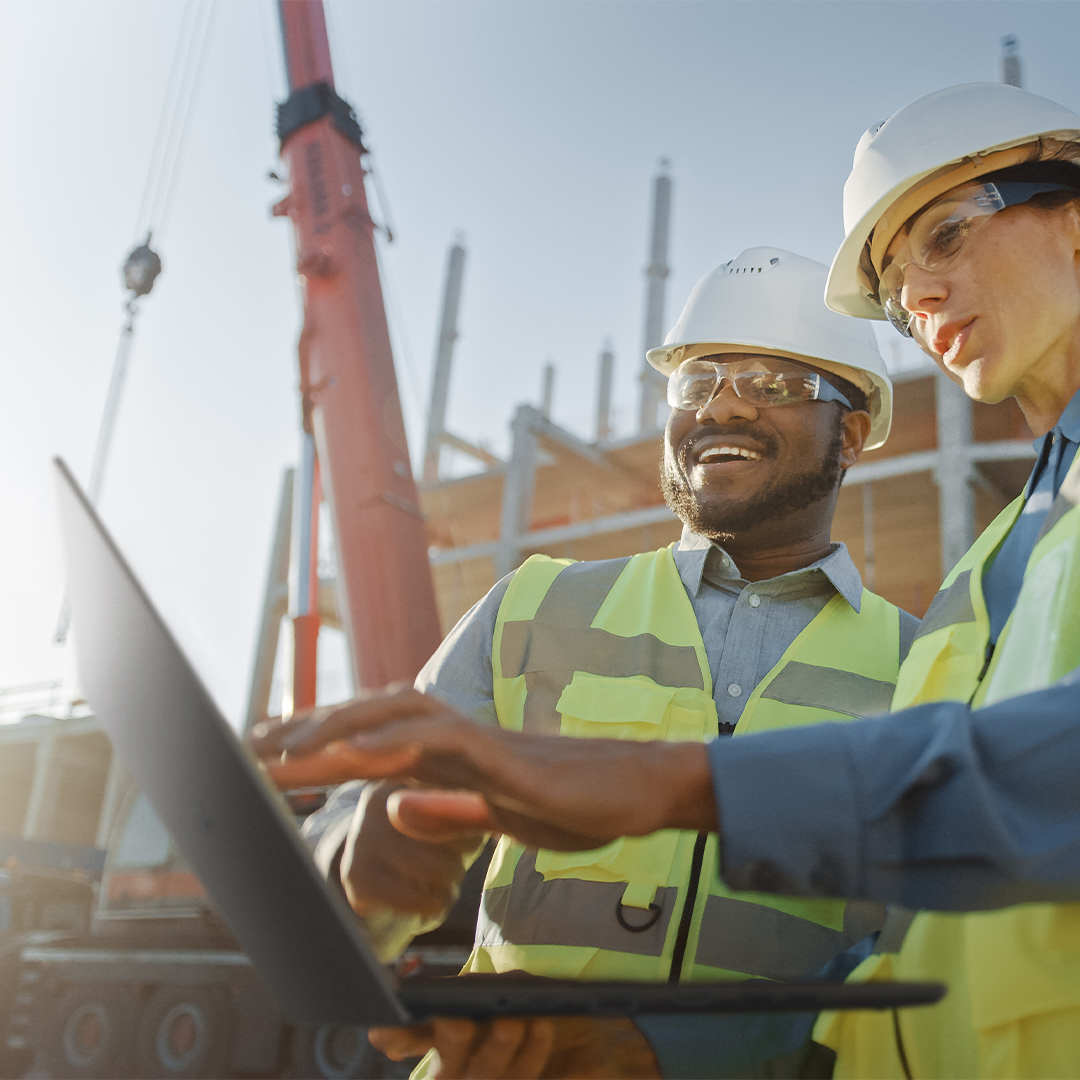 Dos trabajadores de la construcción están revisando algo en la  laptop ASUS ExpertBook en un campo de construcción.