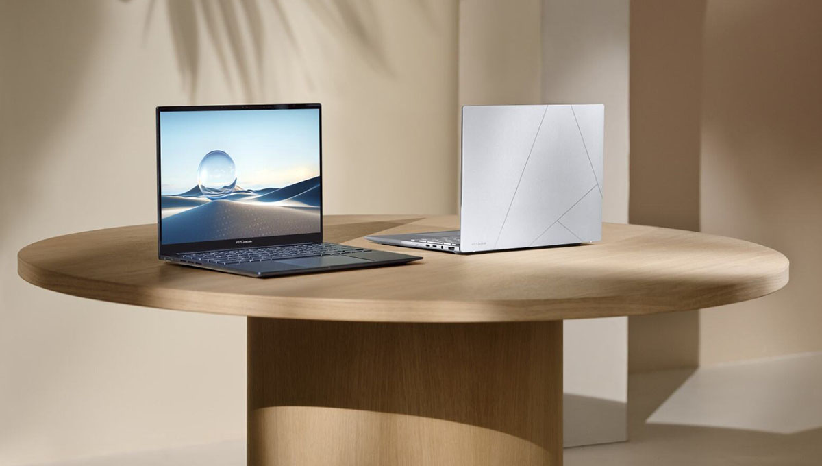 Two ASUS Zenbook 14 laptops are placed on a round wooden table in a calm beige colored setting. The one on the left is front facing while the one on the right faces backwards.