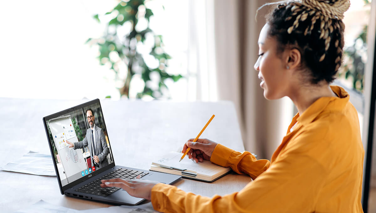 A female student uses an ASUS Vivobook 14 laptop during an online class while taking notes.