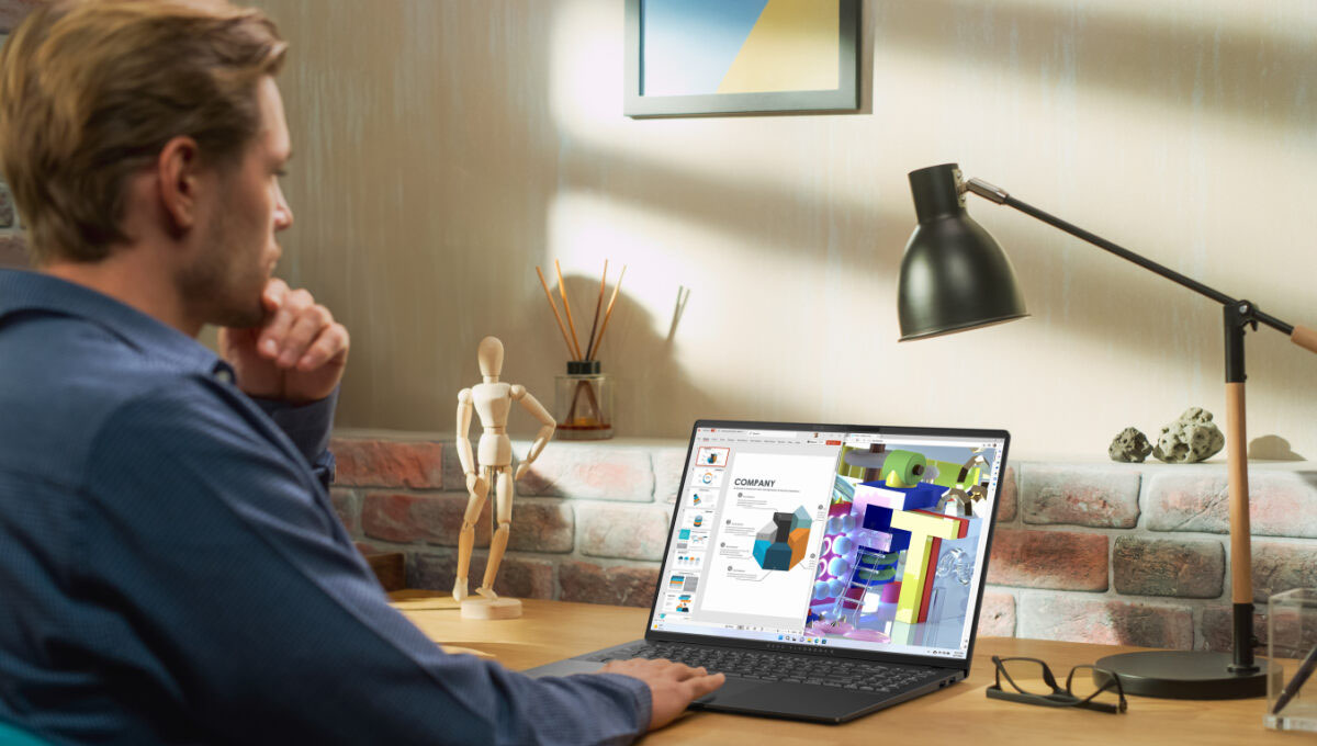 A man sits on at a desk using an ASUS Vivobook S16 laptop, viewing some charts and slides.