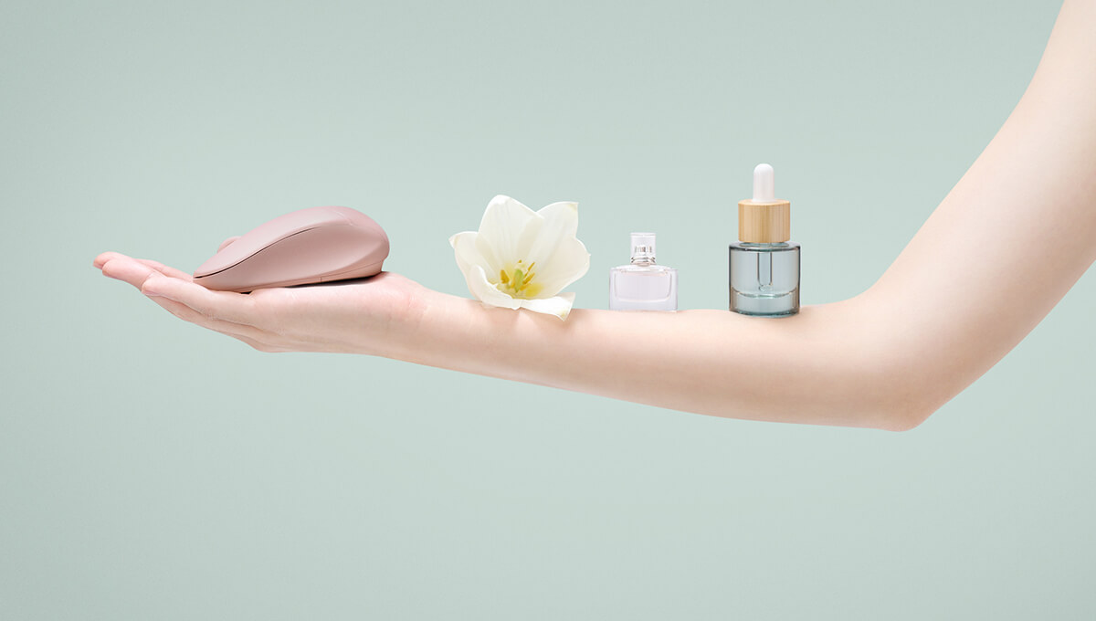 A woman’s arm is extended and on her forearm are balanced an ASUS Fragrance mouse, a flower, a perfume bottle, and an essential oil bottle.