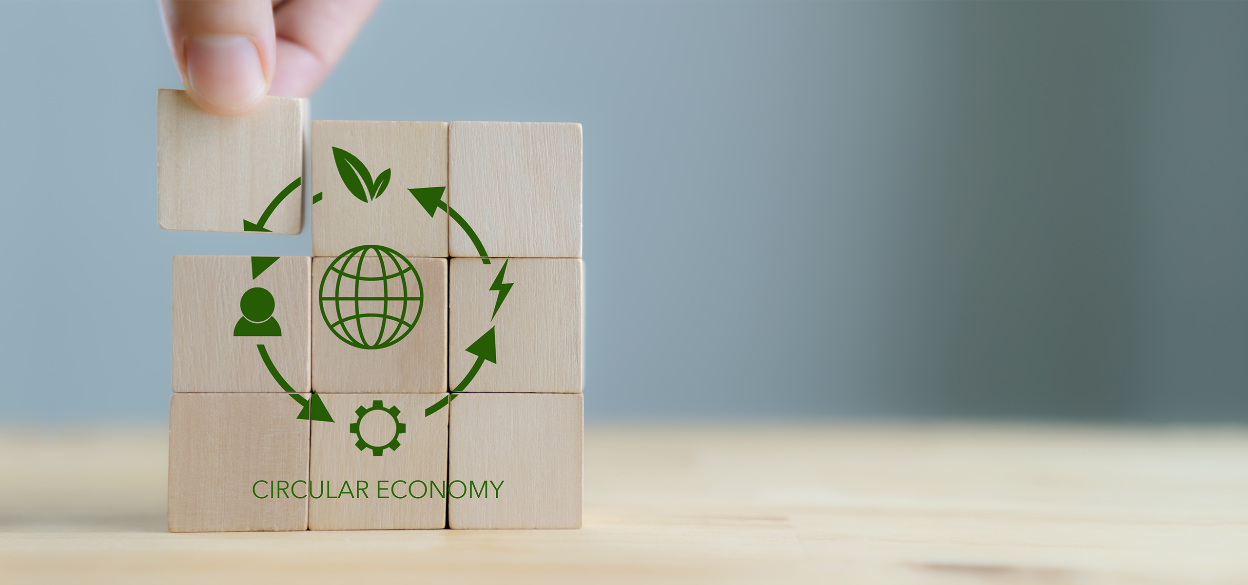 A hand picks up one of the wooden blocks with the words and images 'CIRCULAR ECONOMY' on them