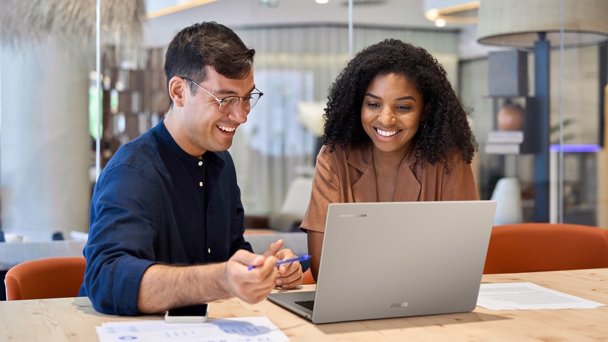 A woman and a man are sitting in front of a desk, discussing work while using the laptop.