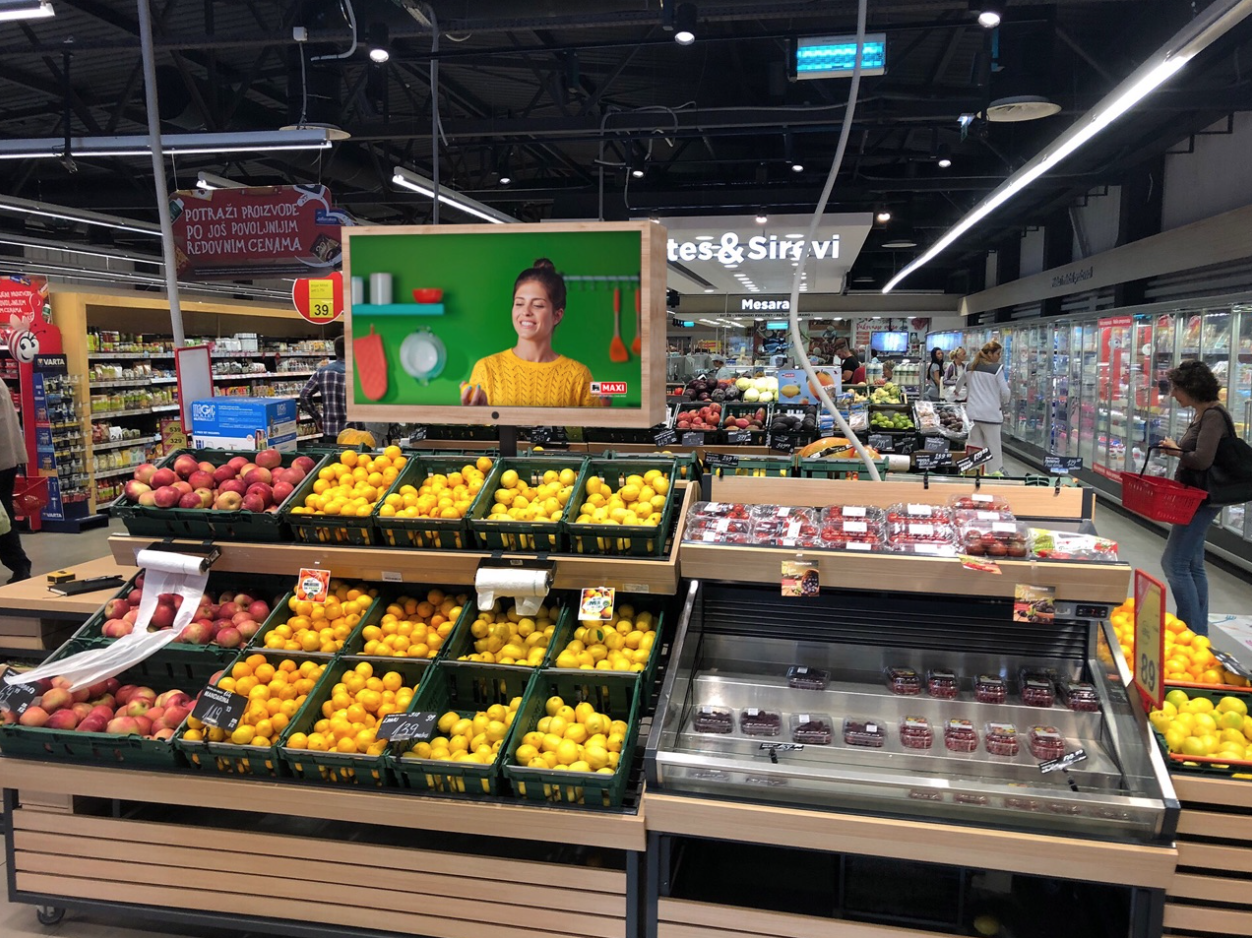 A digital signage display targeted ads in the fruit section of a grocery store