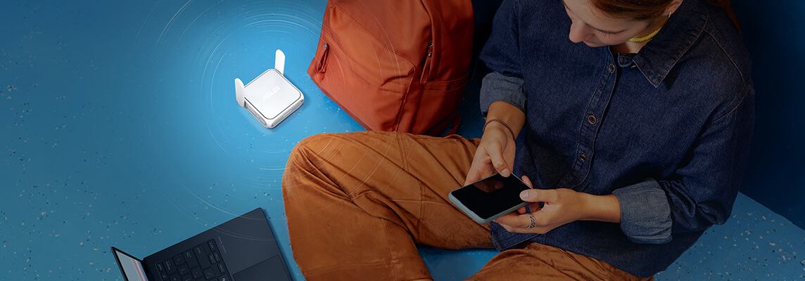 Na podłodze siedzi osoba korzystająca ze smartfona, obok laptopa, pomarańczowego plecaka i białego routera podróżnego WiFi 7.