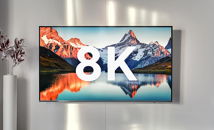 Telewizor z płaskim ekranem wyświetlający napis "8K" na tle krajobrazu gór i jeziora.
