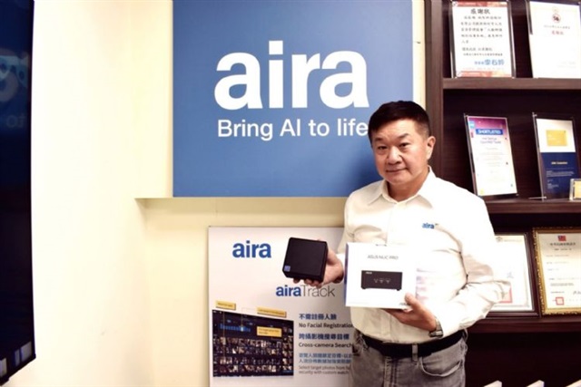 Man posing with a mini PC in front of company logo