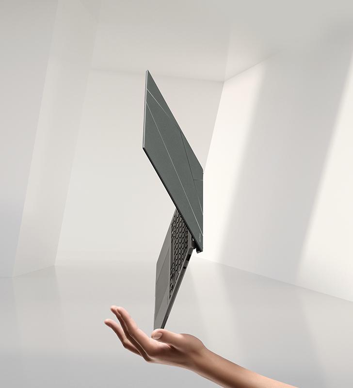 A woman lifts a gray Zenbook S 13 OLED from a stone display stand.
