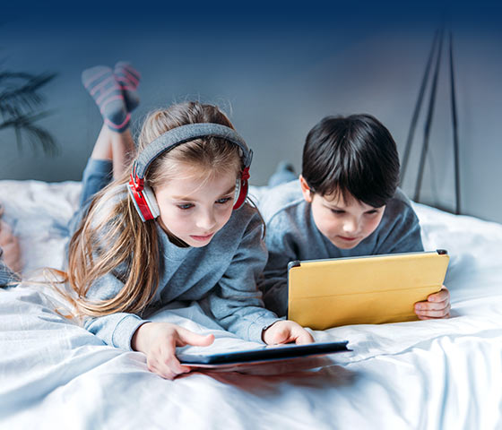 Two children lying on a bed using their tablets