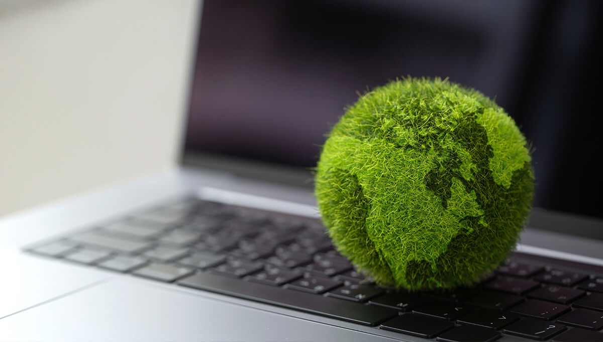 Una bola verde cubierta de musgo ilustrada como la Tierra se encuentra en el teclado de un ordenador portátil.