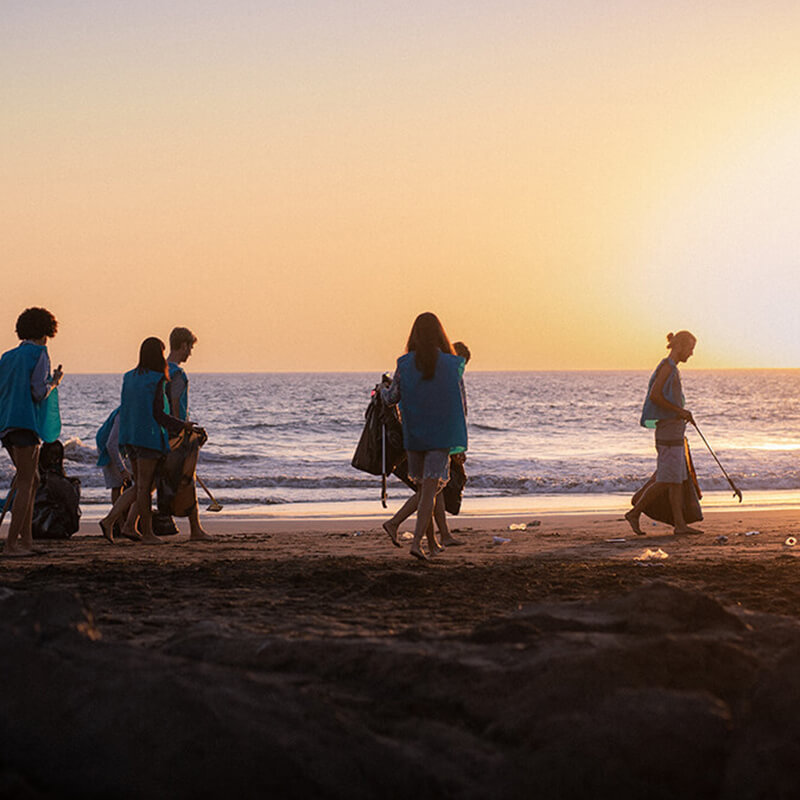 Varias personas recogen basura en la playa mientras el sol se pone de fondo.