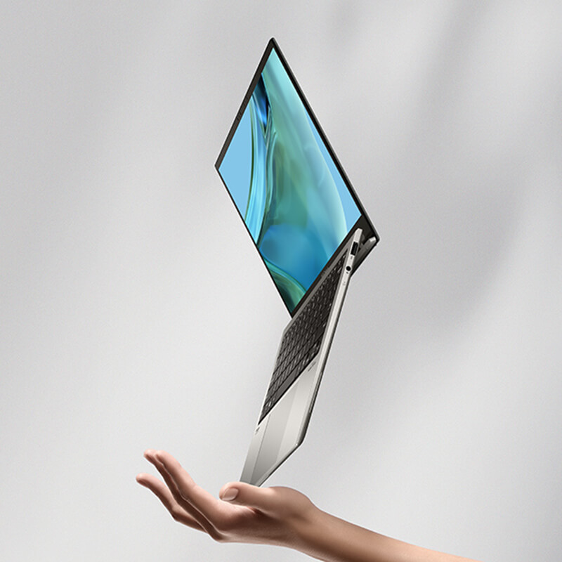 Un ASUS Zenbook A14 gris Islandia está ligeramente abierto y parado en una de sus esquinas, flotando sobre un diente de león.