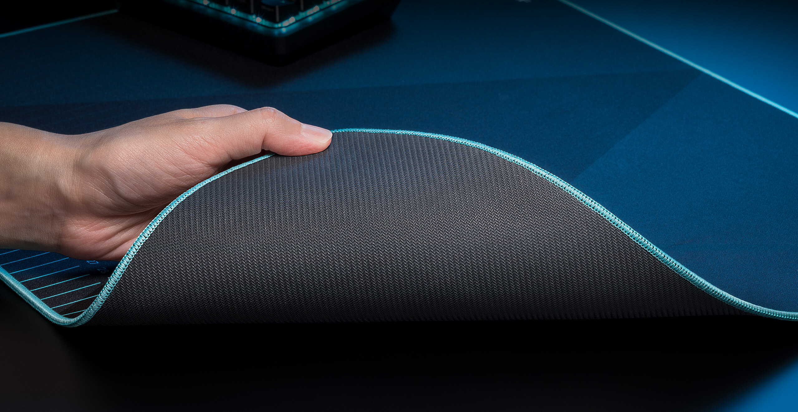 A scenario photo of a hand lifting a corner of the ROG Harpe Ace Aim Lab Edition gaming mouse pad to show the rubber bottom underneath
