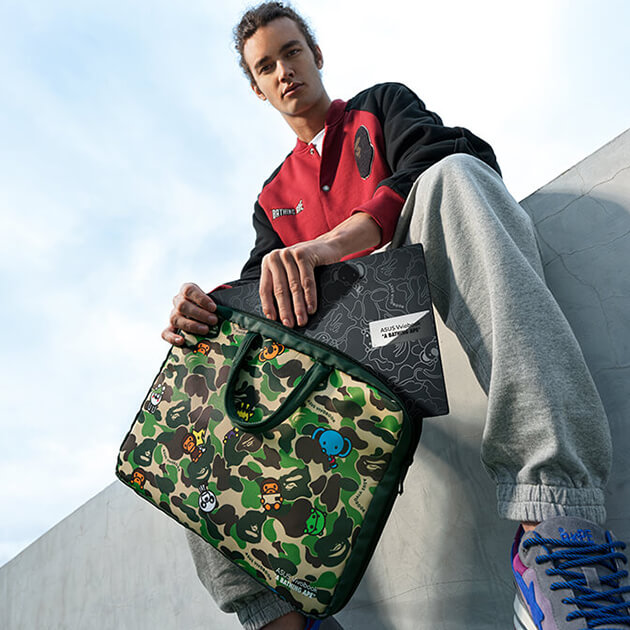 a young man sitting on a wall, dressed in a BAPE outfit, taking the ASUS Vivobook S 15 OLED BAPE Edition out of limited-edition laptop bag