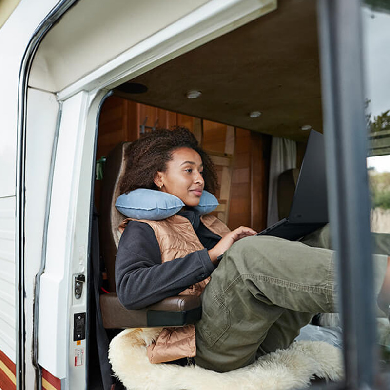 A woman is laid back in her van and using a ProArt P16 laptop with her legs propped up on the dashboard.